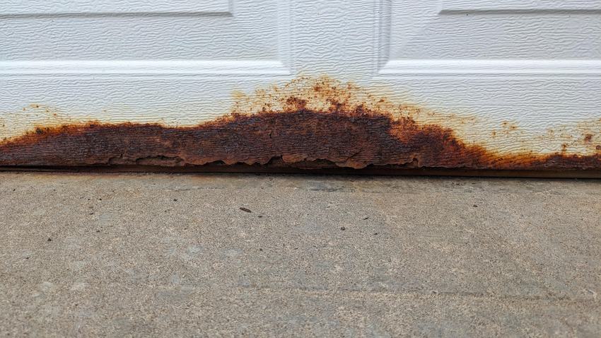 Close-up of severe rust damage on a garage door bottom panel